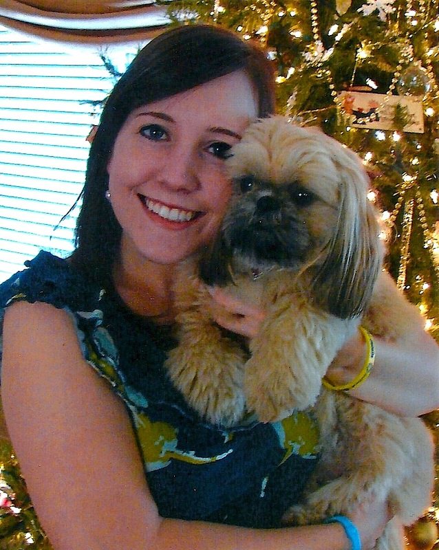 A young woman by a Christmas tree holding a Shih Tzu