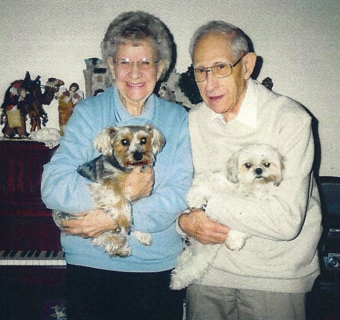 An older couple on a couch, each holding a Shih Tzu