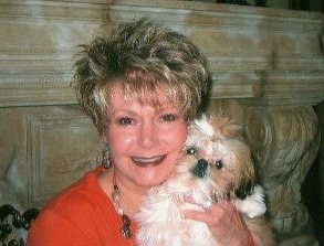 A woman smiling with a small Shih Tzu on her shoulder
